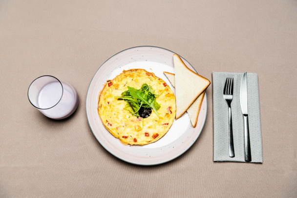 top view of omelet and toasts in plate with fork and knife and glass of yogurt on table  - Foto, Imagem