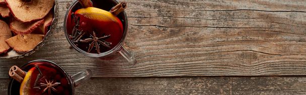 Colpo panoramico di vin brulè speziato rosso con bacche, anice, fette di arancia e cannella su tavolo rustico in legno
 - Foto, immagini