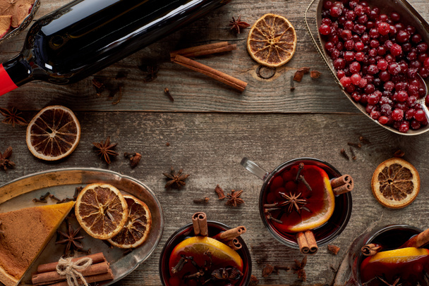 top view of piece of pie, bottle and red spiced mulled wine with berries, anise, orange slices and cinnamon on wooden rustic table - Photo, Image