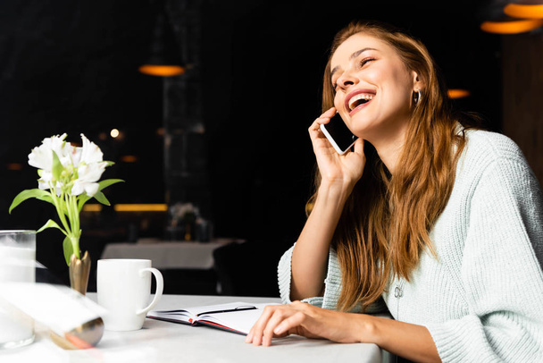 nevető nő beszél okostelefon kávézóban jegyzettömbbel és egy csésze kávét - Fotó, kép