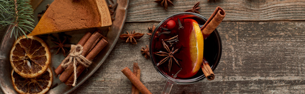 top view of red spiced mulled wine near fir branch, pie, berries, anise, orange slices and cinnamon on wooden rustic table, panoramic shot - Fotó, kép