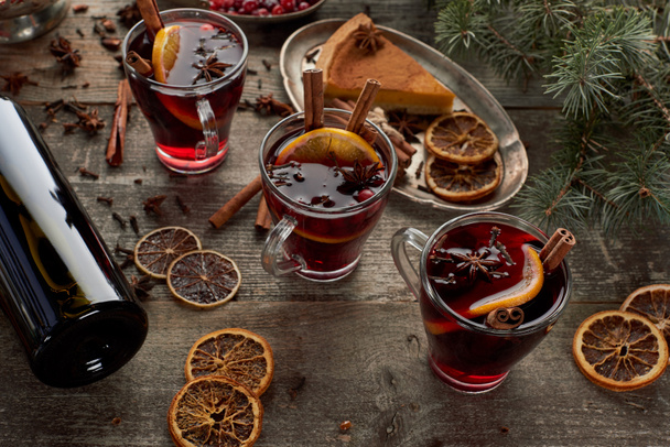 červené kořeněné svařené víno u jedlové větve, koláč, bobule, anýz, pomerančové plátky a skořice na dřevěném rustikálním stole - Fotografie, Obrázek