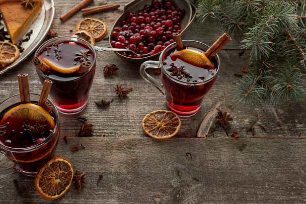 vinho quente picado vermelho perto do ramo de abeto, bagas, anis, fatias de laranja e canela na mesa rústica de madeira
 - Foto, Imagem