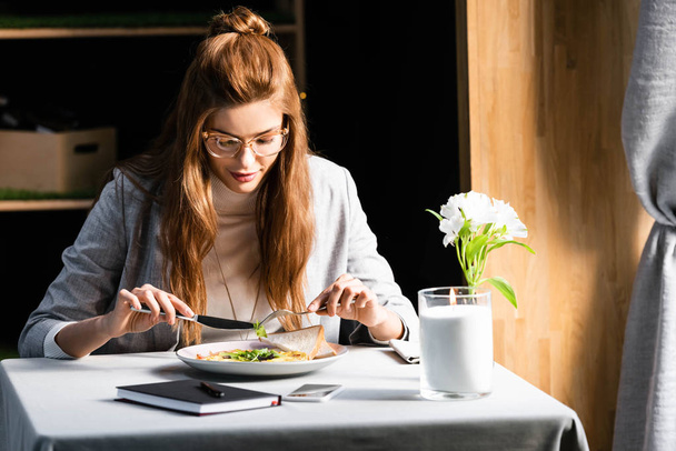 メモ帳やスマートフォンでカフェで朝食を食べる魅力的な女性 - 写真・画像