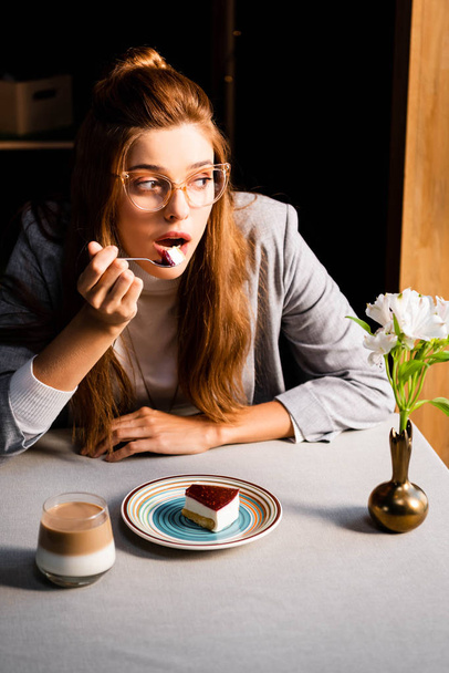 surprised girl eating cake with coffee in cafe with flowers in vase  - Фото, изображение