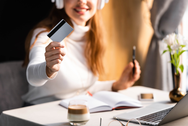 bijgesneden beeld van vrouw in koptelefoon betalen met creditcard in cafe, selectieve focus - Foto, afbeelding