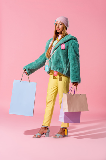 beautiful, stylish african american woman holding shopping bags on pink background, fashion doll concept - Фото, зображення