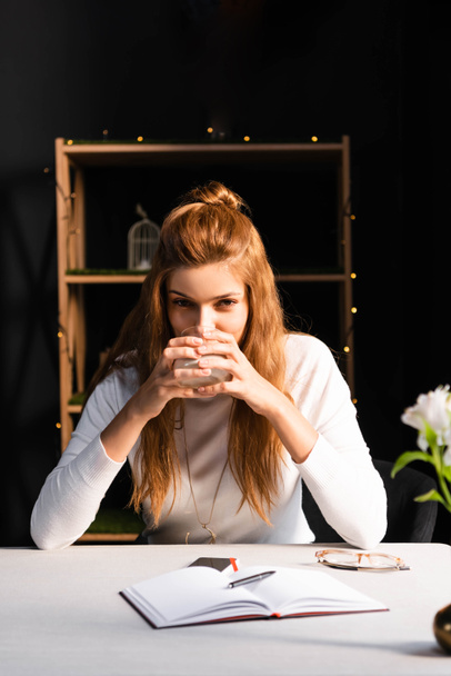 ελκυστική στοχαστική γυναίκα κρατώντας ένα ποτήρι καφέ στο καφέ με σημειωματάριο  - Φωτογραφία, εικόνα