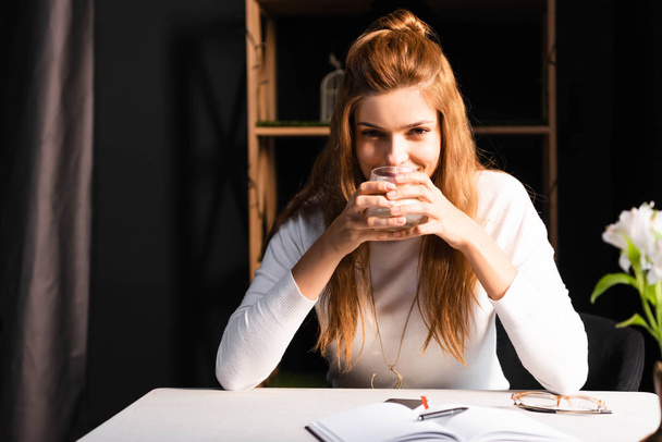 attractive happy woman holding glass of coffee in cafe with notepad  - Photo, Image