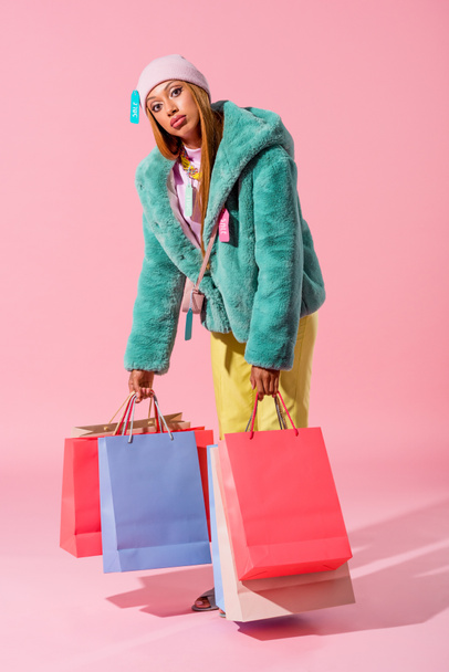 exhausted, fashionable african american woman holding shopping bags on pink background, fashion doll concept - 写真・画像
