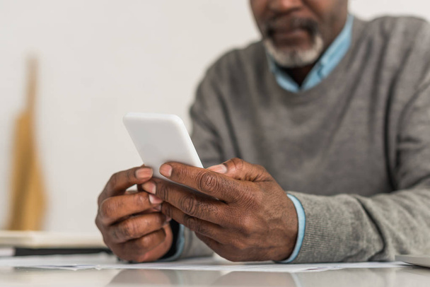 vue recadrée d'un homme afro-américain âgé utilisant un smartphone assis à table
 - Photo, image
