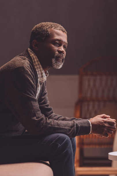 solitário, homem americano africano sênior olhando para longe enquanto sentado no sofá
  - Foto, Imagem