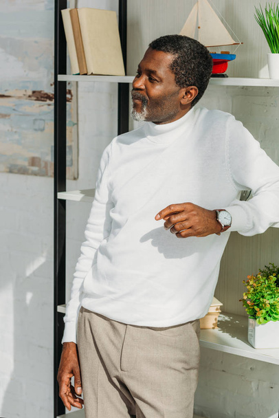 positive african american man in stylish outfit standing near rack and looking away - Photo, Image