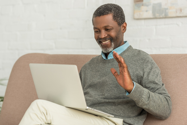 веселий афроамериканський чоловік махає рукою під час відеодзвінка на ноутбук
 - Фото, зображення