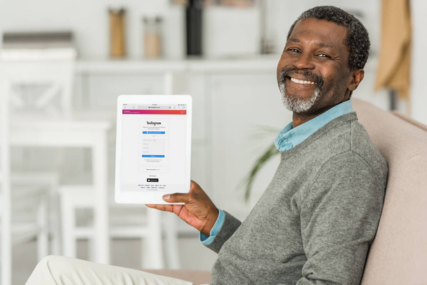 KYIV, UCRANIA - 2 DE OCTUBRE DE 2019: Alegre hombre afroamericano sosteniendo la tableta digital con la aplicación Instagram en la pantalla y sonriendo a la cámara
. - Foto, Imagen