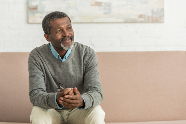 smiling african american man sitting on sofa and looking away - Photo, Image