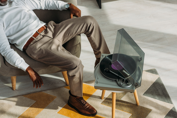 vue recadrée d'un homme afro-américain élégant assis dans un fauteuil et écoutant de la musique sur un tourne-disque
 - Photo, image