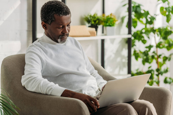 senior african american man sitting in armchair and using laptop - Photo, Image