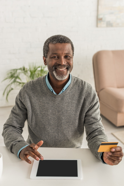 cheerful african american smiling at camera while holding credit card and using laptop - Photo, Image