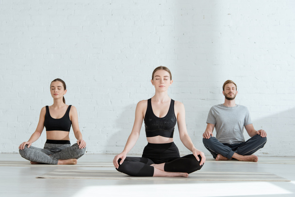 junge Männer und Frauen praktizieren Yoga in halber Lotus-Pose - Foto, Bild