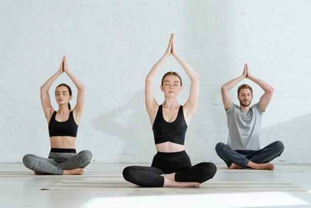giovani uomini e donne che praticano yoga in posa mezzo loto con mani di preghiera sollevate
 - Foto, immagini