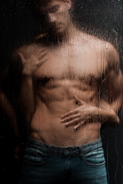 mujer apasionada abrazando hombre sin camisa detrás de vidrio húmedo
 - Foto, Imagen