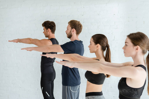 молодые люди в спортивной одежде практикуют йогу в горной позе с протянутыми руками
 - Фото, изображение