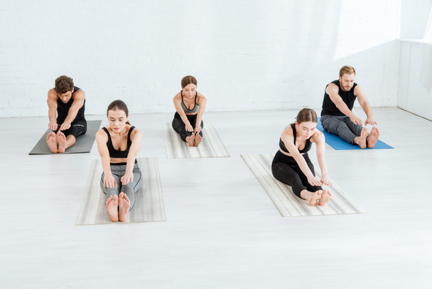 five young people practicing yoga in forward bend pose - Fotó, kép