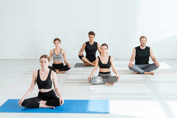 cinco jovens praticando ioga em meia pose de lótus
 - Foto, Imagem