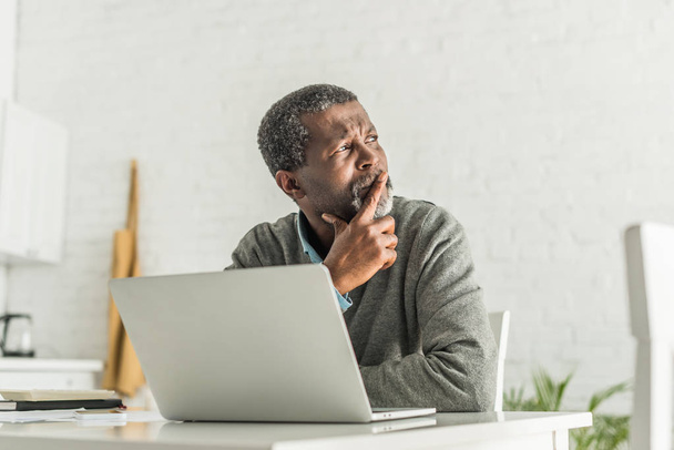 thoughtful african american man looking away while sitting near laptop - Foto, afbeelding