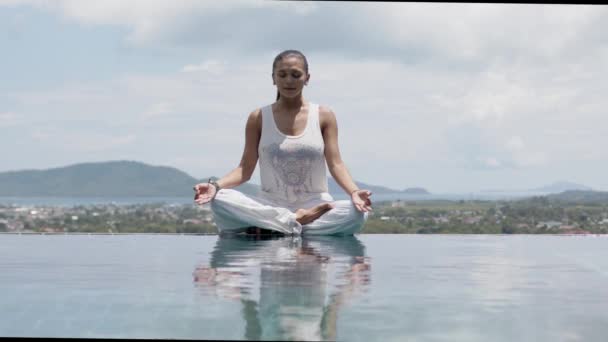 Gelassene Frau praktiziert Yoga in Lotusstellung am Pool gegen den Himmel - Filmmaterial, Video