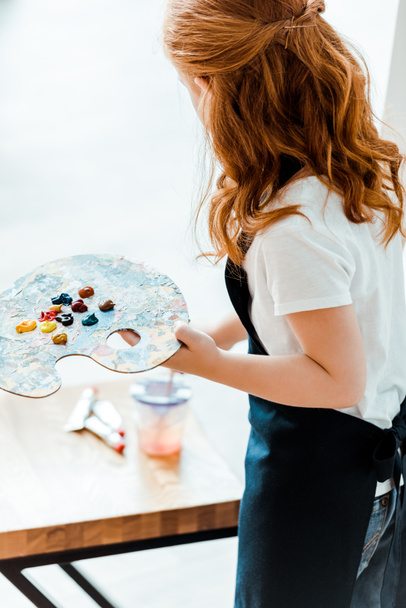 back view of cute redhead kid holding multicolored palette in art school   - Photo, Image