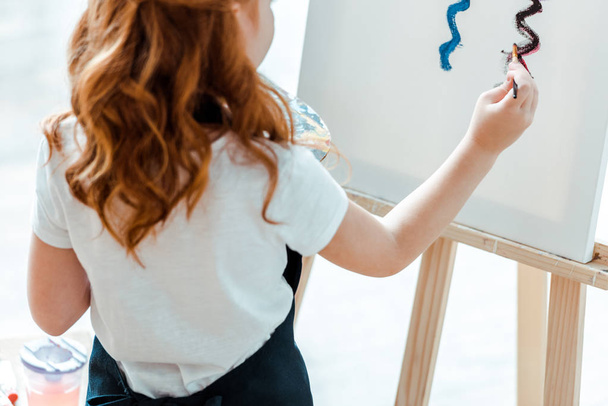 ostříhaný pohled na rusovlasé dítě malování na plátně v umělecké škole  - Fotografie, Obrázek