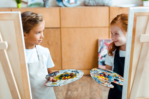 selective focus of kids holding colorful palette and looking at each other  - Photo, Image