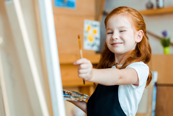 selective focus of happy redhead child holding paintbrush  - Фото, зображення
