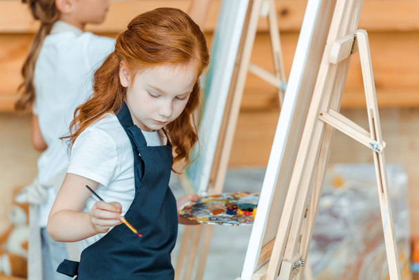 selective focus of cute kid standing and painting in art school  - Foto, afbeelding