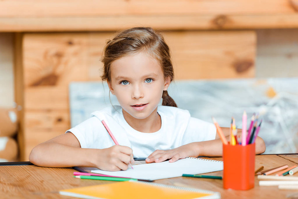 selektywny ostrość słodkie dziecko patrząc w aparat podczas rysowania na papierze w szkole artystycznej  - Zdjęcie, obraz