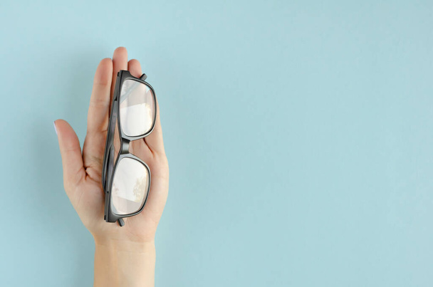 Hand with eyeglasses composition on blue background. - Foto, afbeelding