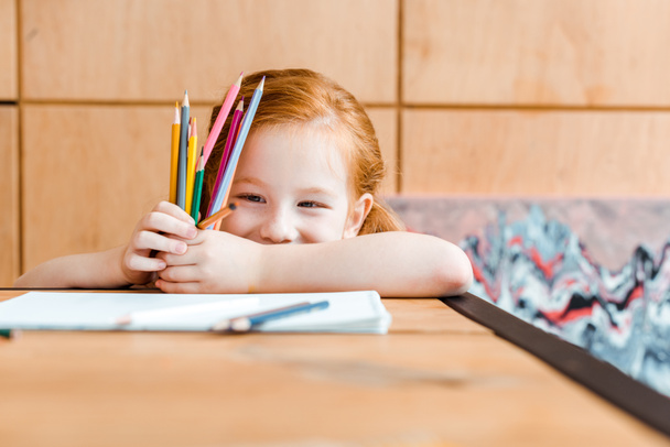 foco seletivo de criança ruiva sorridente segurando lápis de cor
  - Foto, Imagem
