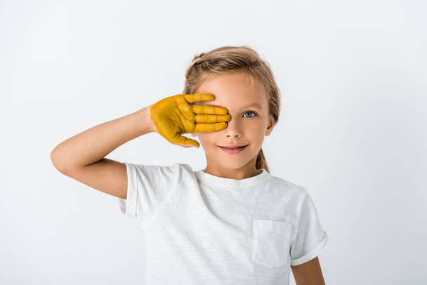 gelukkig kind met gele verf op de hand bedekking gezicht geïsoleerd op wit  - Foto, afbeelding