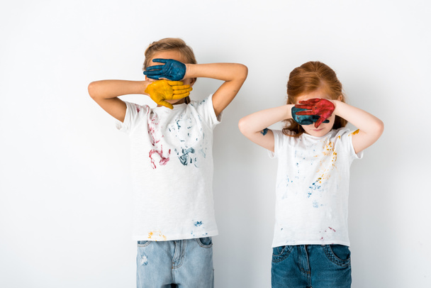 niedliche Kinder mit Farbe auf den Händen, die Gesichter bedeckt, während sie auf weiß stehen  - Foto, Bild