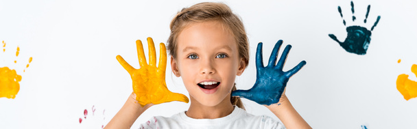 panoramic shot of excited kid with paint on hands near hand prints on white  - Фото, зображення