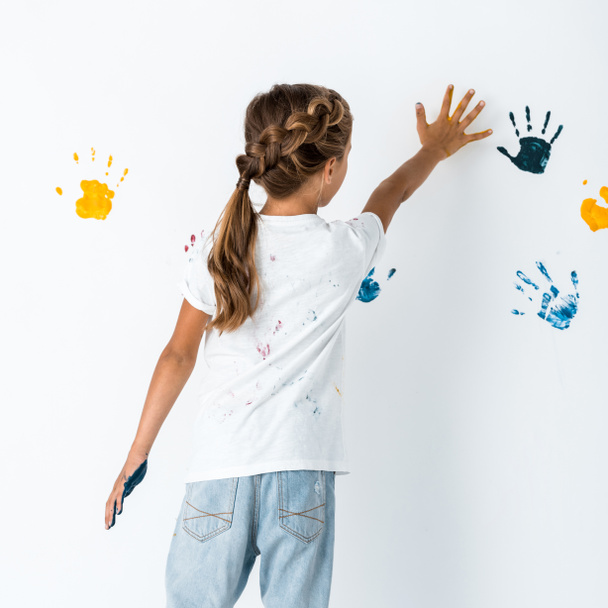 visão traseira da criança colocando a mão perto de impressões de mão no branco
  - Foto, Imagem