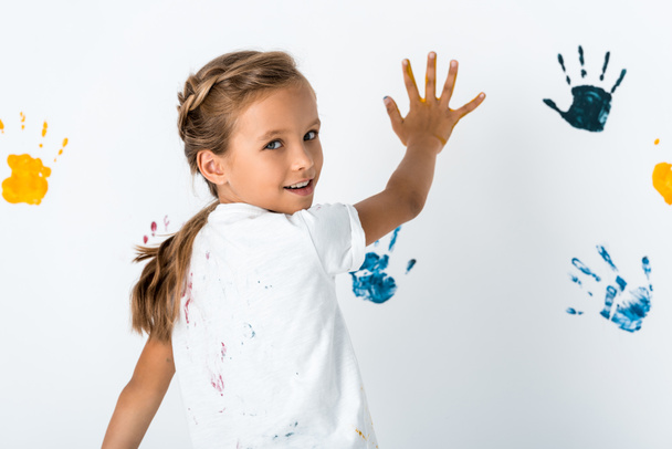 cheerful kid putting hand near hand prints on white  - 写真・画像