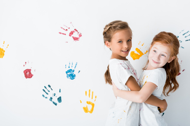 fröhliche Kinder, die sich in der Nähe von Handabdrücken auf Weiß umarmen  - Foto, Bild
