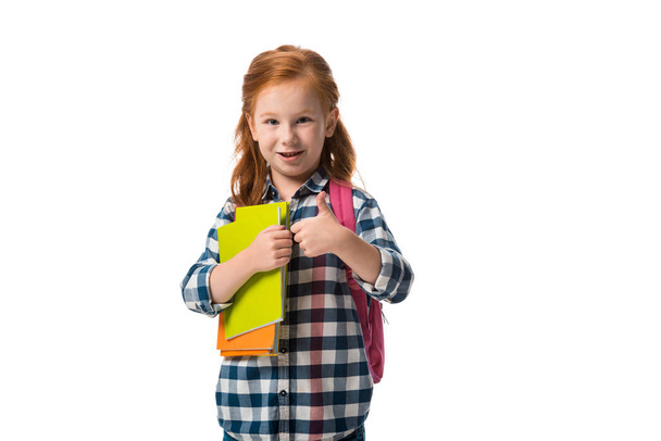 boldog vörös hajú gyerek kezében könyvek és mutatja hüvelykujját fel elszigetelt fehér  - Fotó, kép