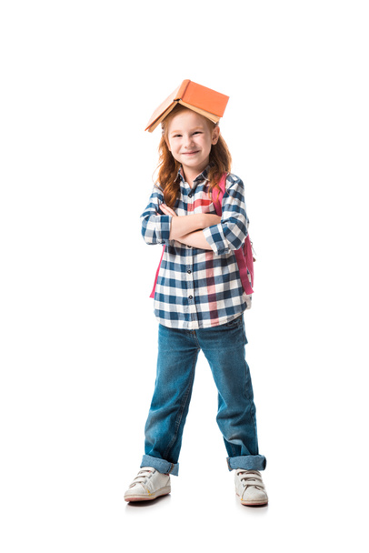 cheerful redhead kid with orange book on head standing with crossed arms isolated on white  - Фото, изображение