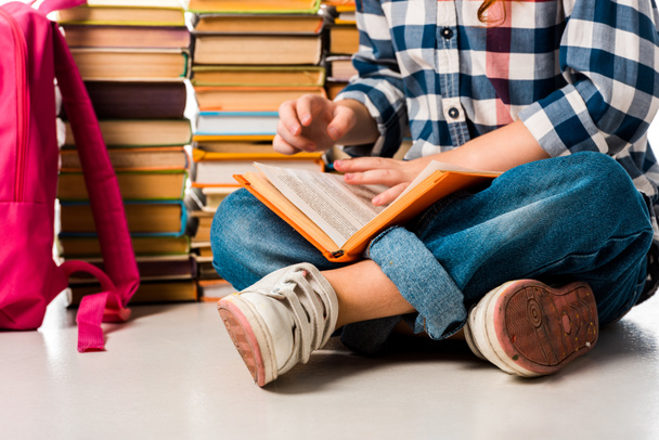 bijgesneden weergave van schoolkind zitten in de buurt van boeken en roze rugzak op wit  - Foto, afbeelding