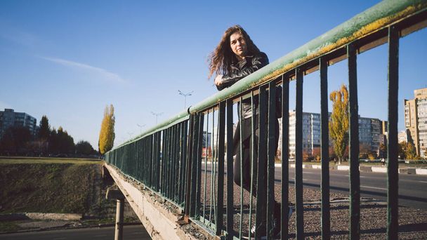 A beautiful young woman stands thoughtfully on the bridge against the background of the urban district. - Fotoğraf, Görsel