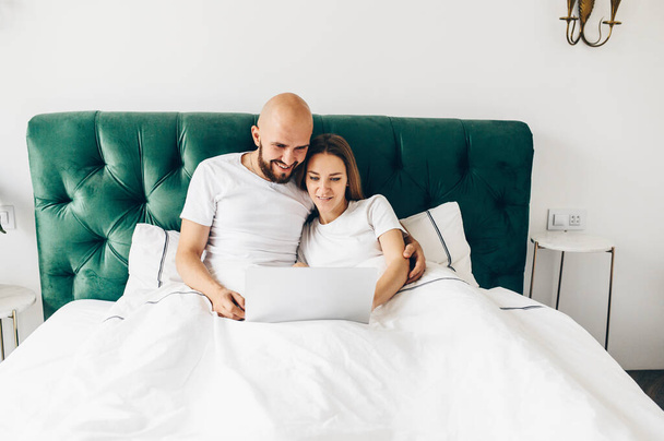 young couple using laptop together in bed  - Foto, afbeelding